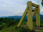 Struktur kayu wahana flying fox yang usang di Bukit Cakrawala Pacitan, dikelilingi rumput liar dengan latar belakang perbukitan hijau dan langit mendung.