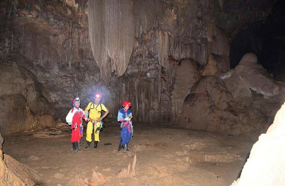 Tiga penjelajah gua lengkap dengan helm dan lampu kepala berdiri di dalam ornamen stalaktit besar Gua Luweng Jaran di Desa Jlubang, Kecamatan Pringkuku, Kabupaten Pacitan.