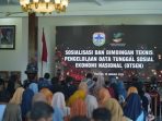 Suasana acara Sosialisasi dan Bimbingan Teknis Pengelolaan Data Tunggal Sosial Ekonomi Nasional (DTSEN) di Pendopo Kabupaten Pacitan pada 29 Januari 2026. Kepala Dinsos Pacitan Heri Setijono berdiri di podium di depan layar besar yang menampilkan judul acara dan logo Pemkab Pacitan serta Kemensos RI, dihadiri oleh audiens yang terdiri dari kepala desa dan operator desa