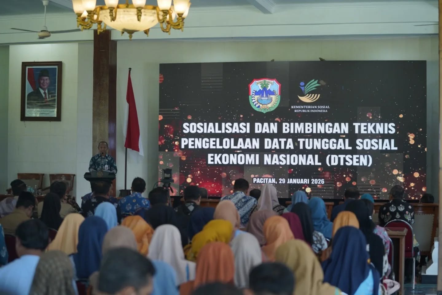 Suasana acara Sosialisasi dan Bimbingan Teknis Pengelolaan Data Tunggal Sosial Ekonomi Nasional (DTSEN) di Pendopo Kabupaten Pacitan pada 29 Januari 2026. Kepala Dinsos Pacitan Heri Setijono berdiri di podium di depan layar besar yang menampilkan judul acara dan logo Pemkab Pacitan serta Kemensos RI, dihadiri oleh audiens yang terdiri dari kepala desa dan operator desa