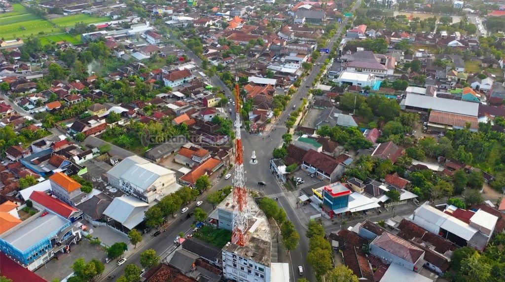 Foto drone udara suasana Perempatan Penceng di Kota Pacitan dengan landmark menara telekomunikasi merah putih di tengah pemukiman padat.
