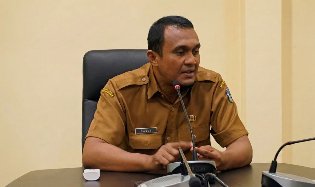 Kepala Bidang Pencegahan dan Kesiapsiagaan BPBD Pacitan, Yagus Triarso, mengenakan seragam cokelat, sedang berbicara ke mikrofon dalam sebuah konferensi pers di ruangan kantor.