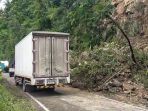 Pengendara motor dan mobil melintas perlahan secara bergantian di area jalan raya Pacitan-Ponorogo yang baru sebagian dibersihkan dari material longsor.