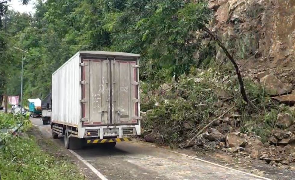 Pengendara motor dan mobil melintas perlahan secara bergantian di area jalan raya Pacitan-Ponorogo yang baru sebagian dibersihkan dari material longsor.