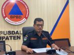 Foto kepala BPBD Kabupaten Pacitan, Erwin Andriatmoko, mengenakan seragam BPBD hitam dan kacamata, sedang memberikan keterangan pers di depan mikrofon di ruang konferensi dengan latar belakang logo BPBD Pacitan pasca gempa Jumat (6/2/2026).