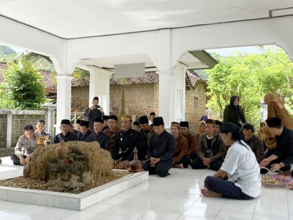 Suasana hening di dalam bangunan makam yang terbuka, di mana sekelompok pria (beberapa berseragam polisi, lainnya berbaju koko atau peranakan) dan wanita berhijab duduk bersila di lantai putih mengelilingi sebuah makam batu, tampak sedang berdoa dengan khidmat.