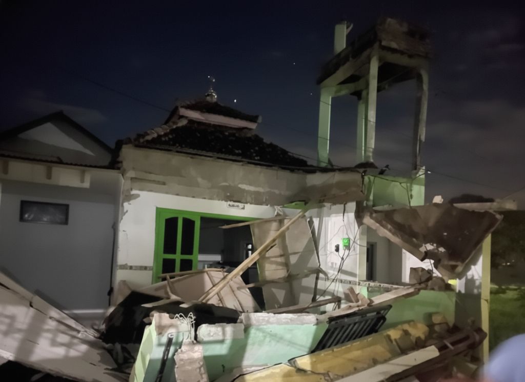 Pemandangan malam hari Musala Al Iman di Pacitan yang hancur; menara dan teras depan roboh dengan puing-puing beton dan kayu berserakan akibat gempa.