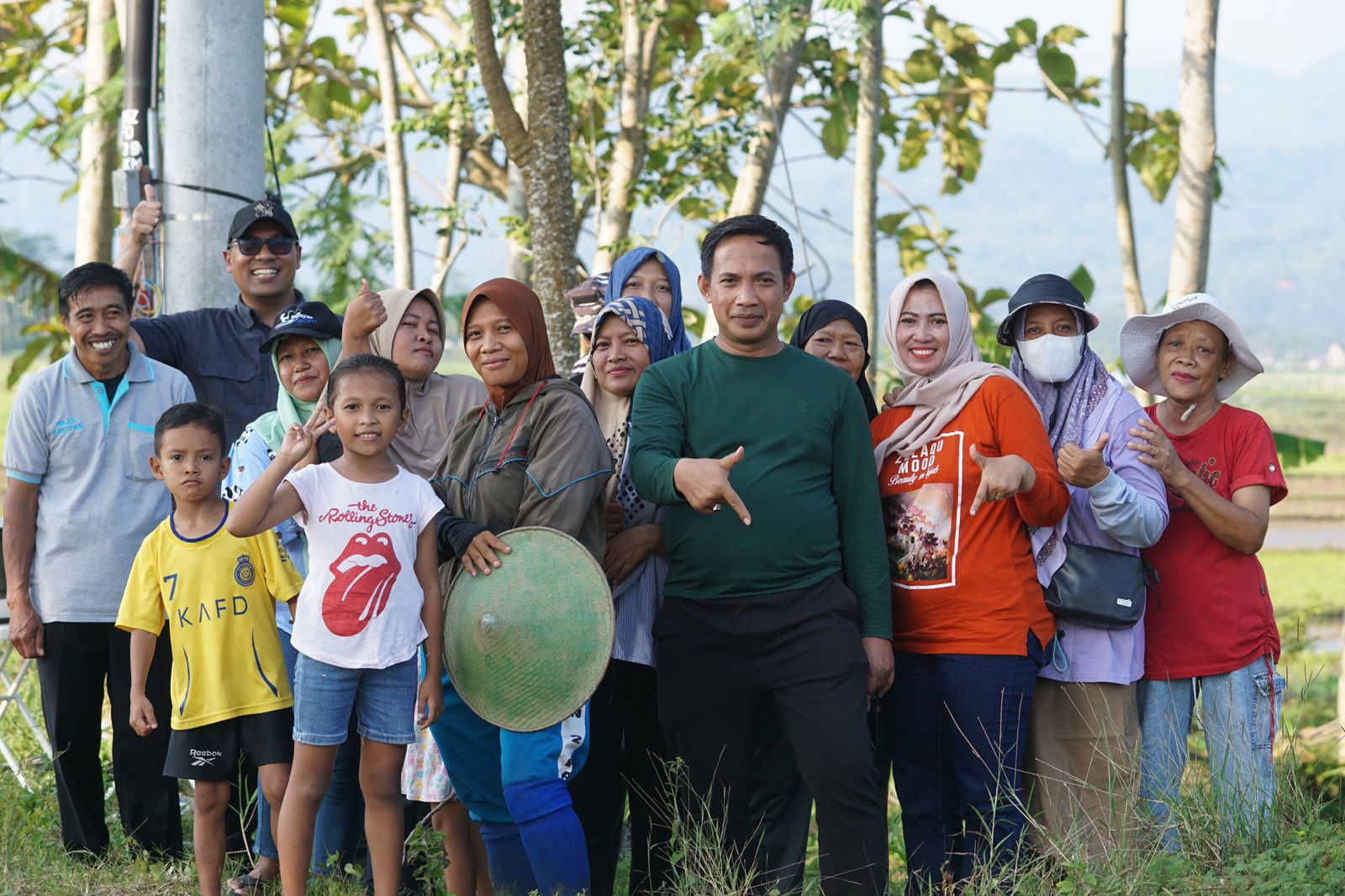 Foto Ketua DPRD Pacitan Arif Setia Budi (tengah, kemeja hijau) berpose akrab bersama warga dan anak-anak di area persawahan Pacitan, dengan latar belakang pohon dan bukit.