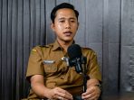 Khrisna Adi Pradana, seorang guru dan kreator konten edukasi asal Pacitan, mengenakan seragam dinas khaki (ASN) dan duduk di depan mikrofon saat menjadi narasumber dalam siniar (podcast) Kertas Kosong.