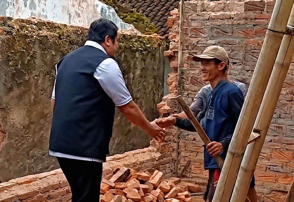 Wakil Bupati Pacitan, Gagarin, mengenakan rompi hitam sedang bersalaman dengan seorang warga pria di tengah reruntuhan bangunan rumah akibat gempa bumi di Lingkungan Gantung.