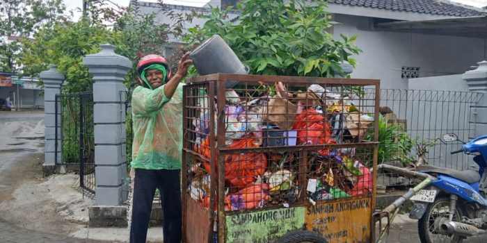Pak Tono petugas kebersihan Pacitan memakai jas hujan plastik sedang mengangkut sampah warga
