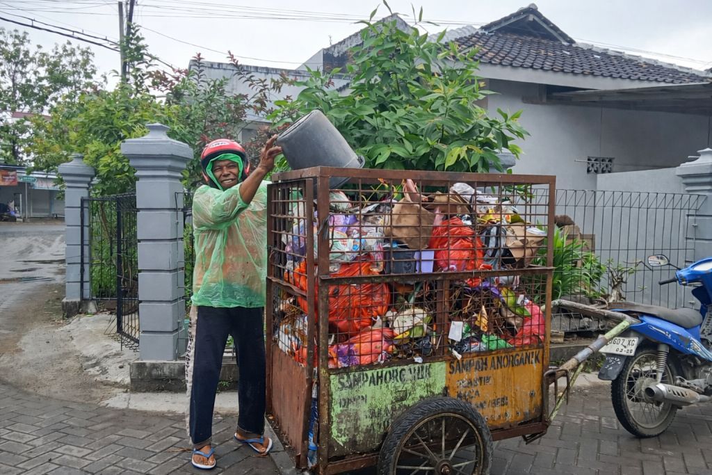 Pak Tono petugas kebersihan Pacitan memakai jas hujan plastik sedang mengangkut sampah warga