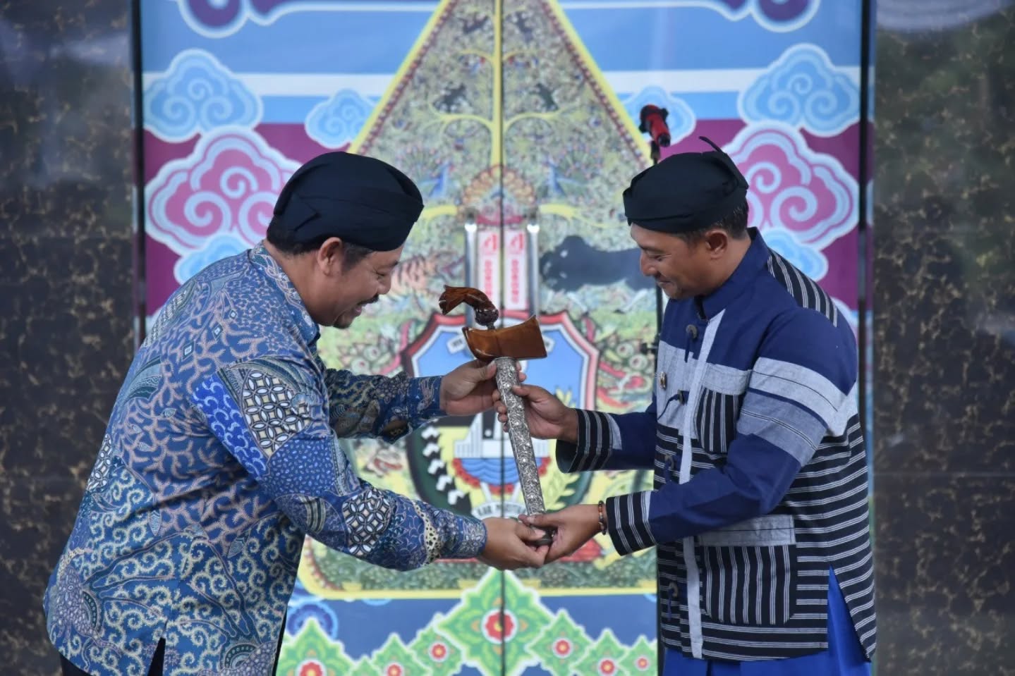 Dua pria mengenakan busana tradisional Jawa dan blangkon melakukan prosesi serah terima keris secara simbolis dalam acara pembukaan pameran Gelar Budaya Luwung di Pacitan, yang menampilkan keris pusaka milik Presiden Prabowo Subianto.