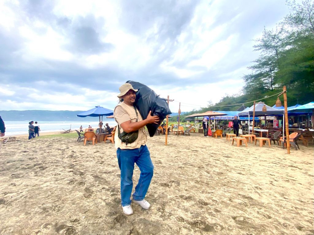 Seorang anggota Forum Pewarta Pacitan (FPPA) memanggul kantong plastik hitam besar berisi sampah saat aksi bersih-bersih pantai di kawasan wisata Pancer Door, Pacitan, dalam rangka memperingati Hari Pers Nasional (HPN) ke-80.