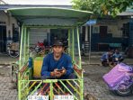 Mujiono, seorang pengemudi becak motor lanjut usia, duduk beristirahat di atas kendaraannya sambil menunggu penumpang di kawasan Pasar Minulyo, Pacitan.