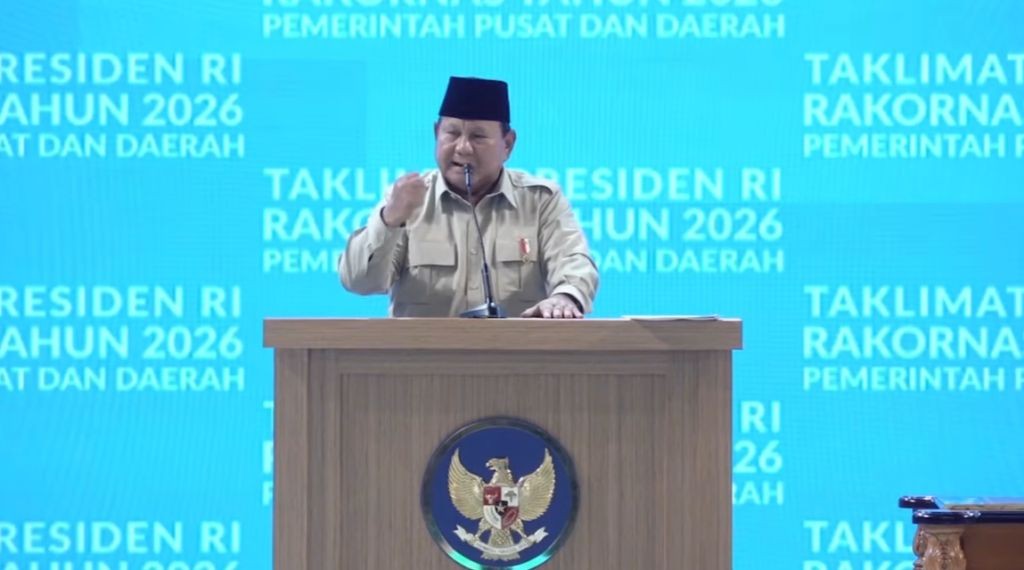 Presiden Prabowo Subianto, mengenakan seragam dinas harian berwarna cokelat dan peci hitam, berbicara di mimbar berlogo Garuda Pancasila saat mencanangkan proyek gentengisasi nasional dalam Rapat Koordinasi Nasional (Rakornas) Pemerintah Pusat dan Daerah Tahun 2026 di Sentul, Senin (2/2/2026). Latar belakang menunjukkan tulisan "RAKORNAS TAHUN 2026" dan "PEMERINTAH PUSAT DAN DAERAH".