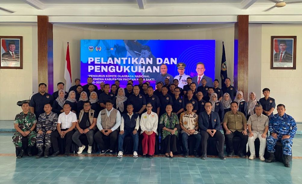 Foto bersama jajaran pengurus Komite Olahraga Nasional Indonesia (KONI) Kabupaten Pacitan masa bakti 2025–2029 yang mengenakan seragam biru tua dan beberapa di antaranya berseragam dinas TNI/Polri, berpose di depan panggung pelantikan di Pendopo Kabupaten Pacitan dengan latar belakang layar LED bertuliskan "PELANTIKAN DAN PENGUKUHAN PENGURUS KONI KABUPATEN PACITAN".