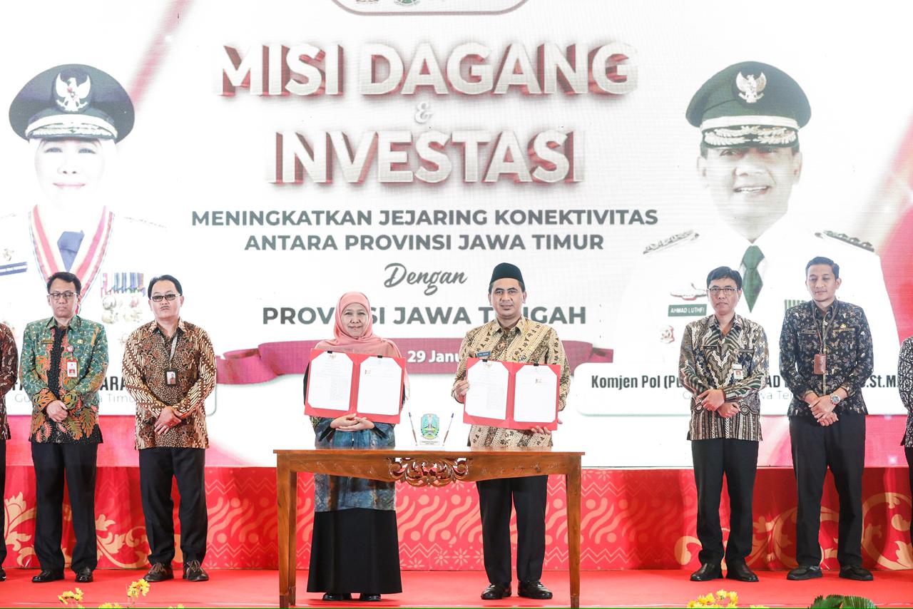 Suasana panggung utama acara Misi Dagang dan Investasi antara Provinsi Jawa Timur dan Jawa Tengah. Terlihat Gubernur Khofifah Indar Parawansa (kiri) dan Wakil Gubernur Taj Yasin Maimoen (kanan) memegang dokumen perjanjian di belakang meja, dengan latar belakang layar besar bergambar foto mereka dan tulisan "MISI DAGANG & INVESTASI".