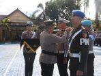 Suasana apel gelar pasukan di lapangan di mana perwira polisi menyematkan pita operasi kepada anggota TNI (Polisi Militer) disaksikan barisan personel lainnya.