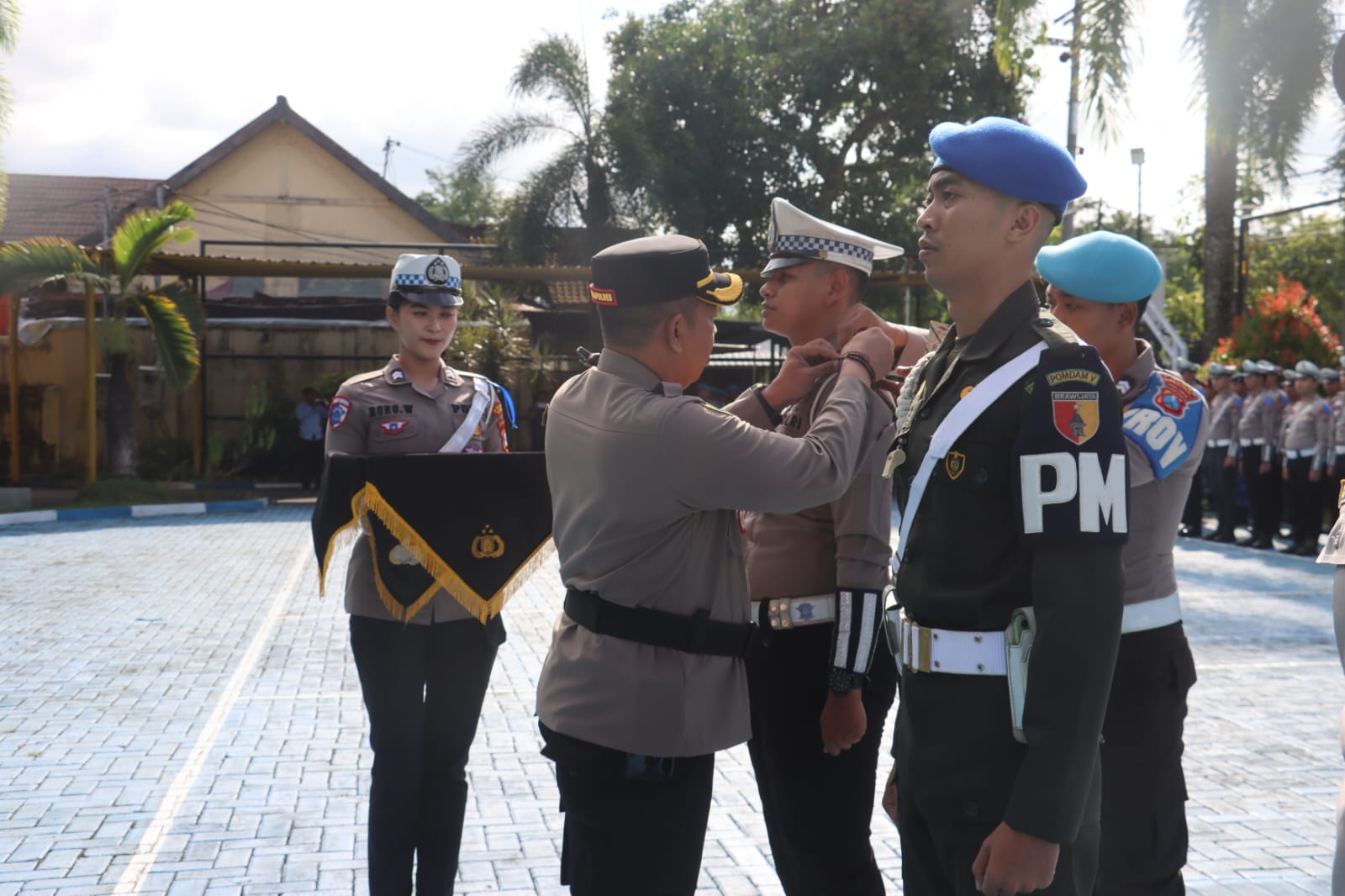 Suasana apel gelar pasukan di lapangan di mana perwira polisi menyematkan pita operasi kepada anggota TNI (Polisi Militer) disaksikan barisan personel lainnya.