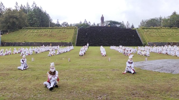 Sebanyak 281 siswa SMAN 1 Nawangan mengenakan kostum Kethek Ogleng putih duduk di lapangan rumput di depan Monumen Jenderal Soedirman di Pacitan, Jawa Timur. Mereka membentuk formasi di depan tangga hitam besar yang mengarah ke patung Jenderal Soedirman di puncak bukit.