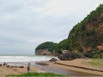Pemandangan hamparan pasir, deburan ombak, dan tebing megah yang mengelilingi kawasan asri Pantai Taman di Desa Hadiwarno, Pacitan.