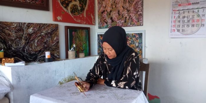 Close-up tangan Sumarni Rahayu menggoreskan canting dengan lilin panas di atas kain putih untuk membuat Batik Chanting Pace.