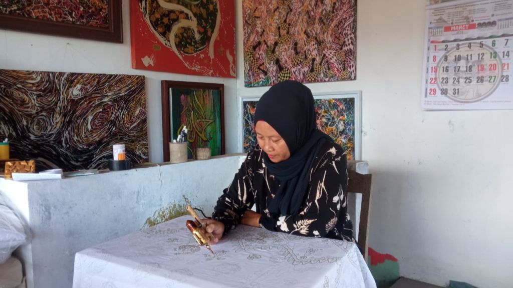 Close-up tangan Sumarni Rahayu menggoreskan canting dengan lilin panas di atas kain putih untuk membuat Batik Chanting Pace.