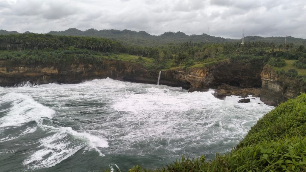 Pemandangan lubang karang alami di Pantai Karang Bolong Pacitan dilihat dari atas tebing terjal.