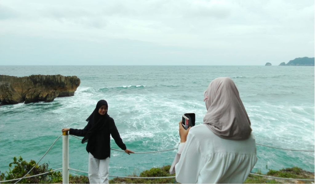 Deburan ombak besar menghantam tebing karang hijau di Pantai Watu Bale Pacitan.