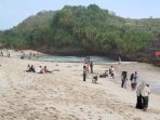 Sejumlah wisatawan berjalan-jalan dan duduk santai di hamparan pasir putih Pantai Srau, Pacitan, dengan latar belakang deburan ombak dan tebing karang pada H+3 libur Lebaran.