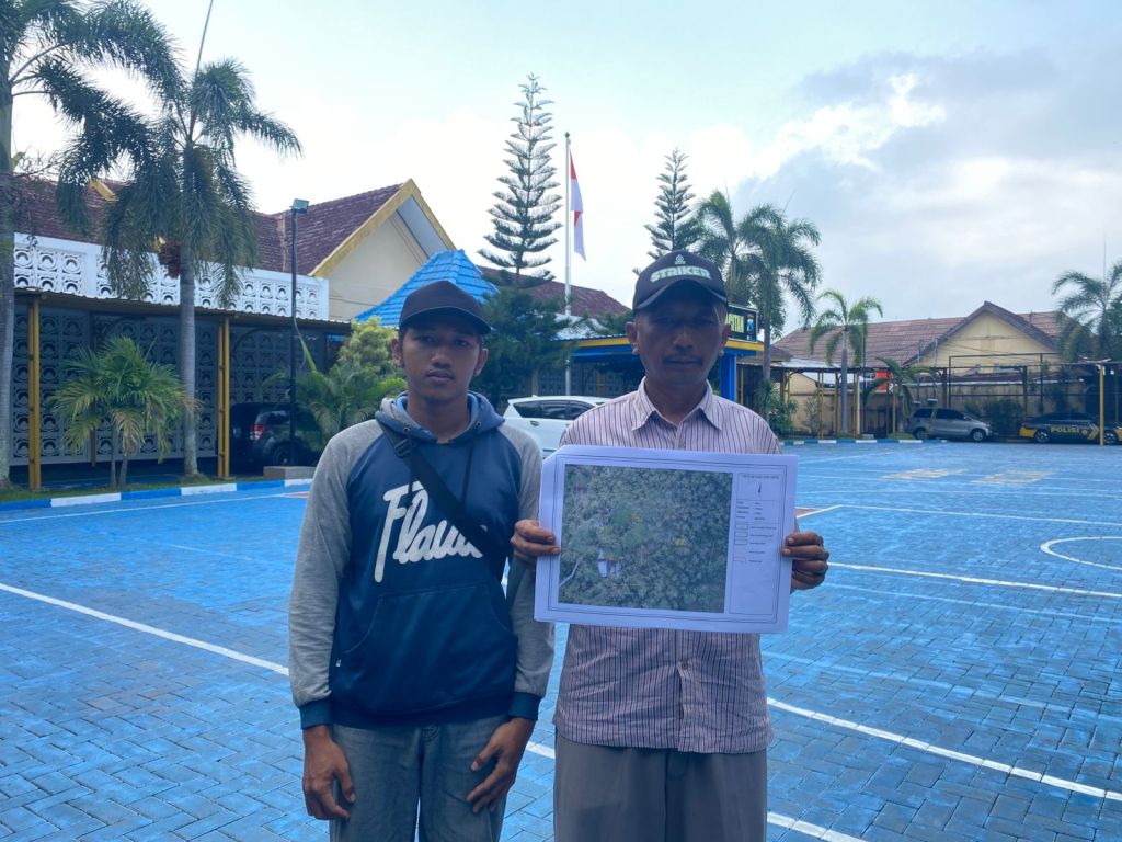 Kateni didampingi anakanya menunjukkan dokumen peta tanah hasil ukur ulang BPN di halaman Mapolres Pacitan.