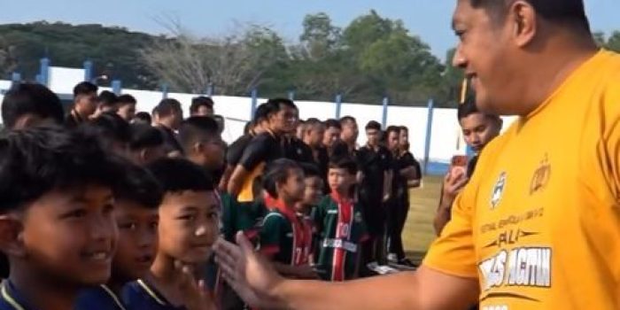 Wakil Bupati Pacitan Gagarin tersenyum sambil melakukan 'tos' high-five dengan anak peserta turnamen sepak bola usia dini di lapangan.