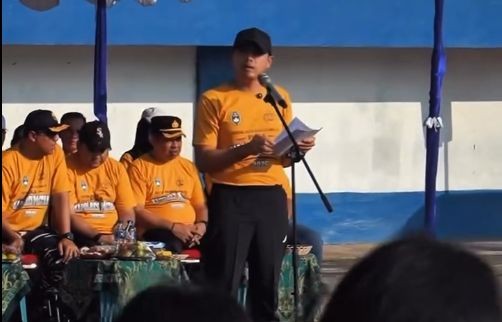 Kapolres Pacitan berdiri di podium memegang mikrofon memberikan sambutan pembukaan di tengah lapangan sepak bola.