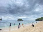 Wisatawan Menikmati Keindahan Sore Pantai Watu Karung Pacitan Wisatawan bersantai di Pantai Watu Karung, Pringkuku, Pacitan, pada sore hari, menampilkan tebing karang ikonik dan peselancar.
