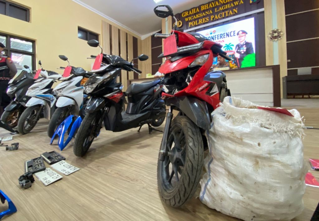 Barang Bukti Pencurian Umbi Porang Pacitan Foto barang bukti kasus pencurian umbi porang di Polres Pacitan. Di sebelah kanan, terlihat satu karung putih berisi umbi porang yang penuh dan sepeda motor Honda Beat warna hitam yang digunakan pelaku. Di area tengah, terdapat tas selempang, pisau, dompet, KTP, dan tumpukan nota penjualan porang yang tersusun rapi.
