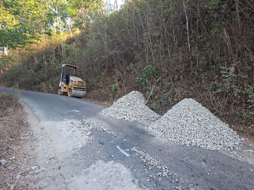 Alat berat dan tumpukan material batu koral serta aspal bersiaga di tepi jalan rusak kawasan Sengkan Selang, Tegalombo, Pacitan.