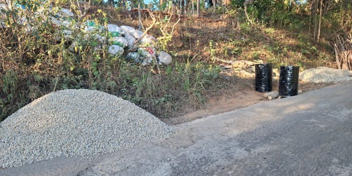 Alat berat dan tumpukan material batu koral serta aspal bersiaga di tepi jalan rusak kawasan Sengkan Selang, Tegalombo, Pacitan.