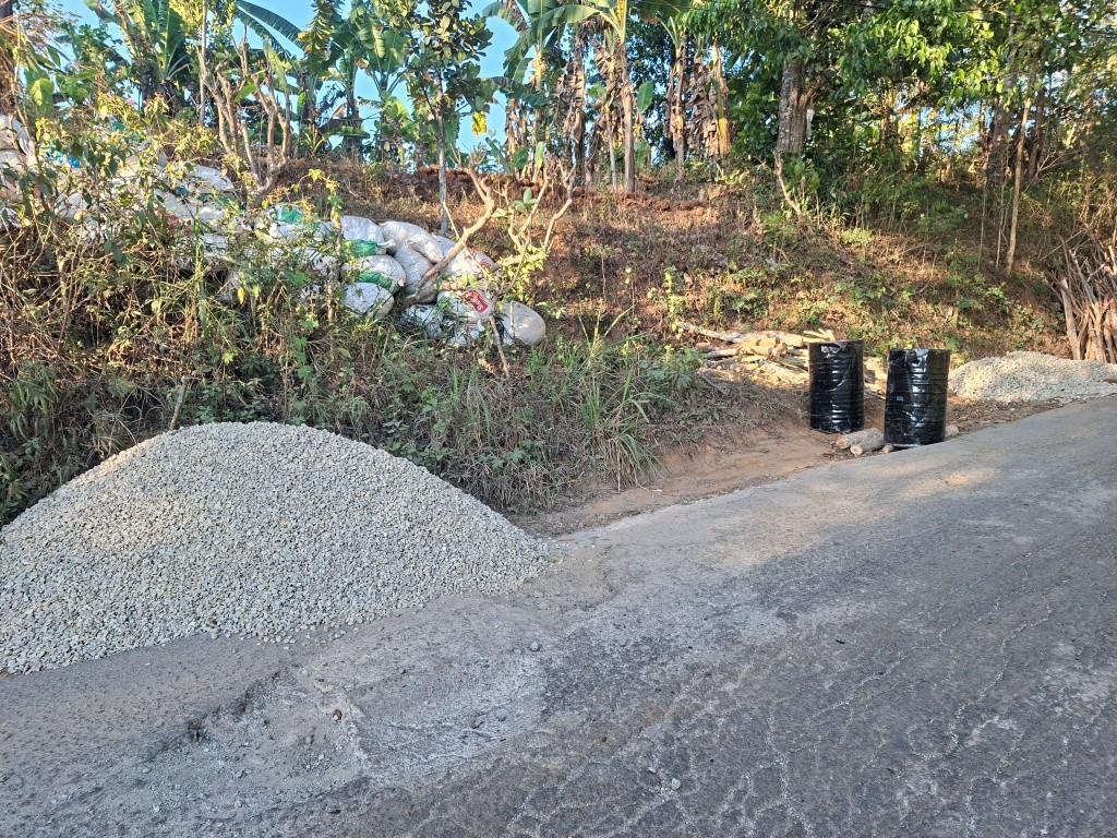Alat berat dan tumpukan material batu koral serta aspal bersiaga di tepi jalan rusak kawasan Sengkan Selang, Tegalombo, Pacitan.