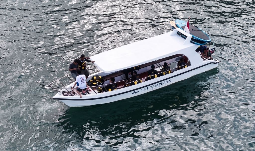 Citra Udara The Tamperan Cruise Mengarungi Teluk Pacitan Pemandangan udara (drone) sudut tinggi kapal wisata The Tamperan Cruise berwarna putih sedang meluncur di perairan Teluk Pacitan dengan latar belakang tebing karang dan pantai.