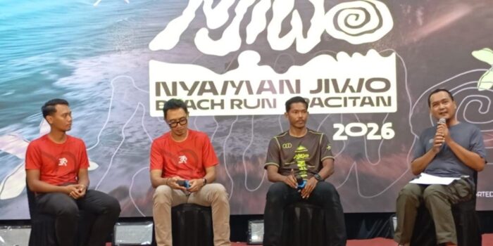 Jurnalis senior Purwoto memegang mikrofon saat berbincang dengan atlet ultra trail Rachmat Septiyanto (Mas Jon) dan jajaran panitia peluncuran Nyaman Jiwo Beach Run Pacitan 2026 di atas panggung.
