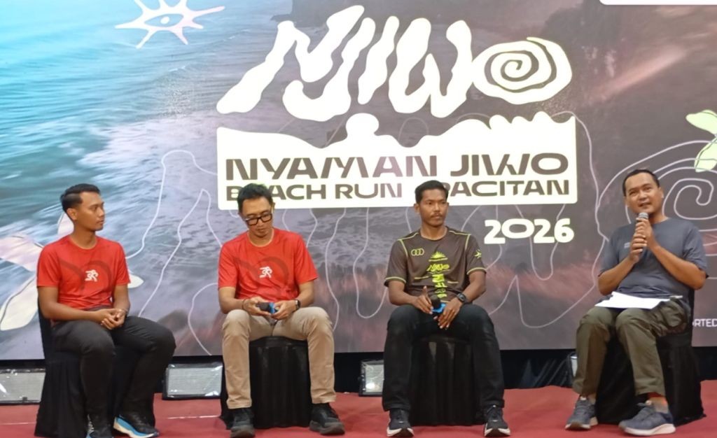 Jurnalis senior Purwoto memegang mikrofon saat berbincang dengan atlet ultra trail Rachmat Septiyanto (Mas Jon) dan jajaran panitia peluncuran Nyaman Jiwo Beach Run Pacitan 2026 di atas panggung.