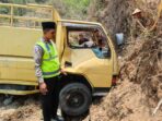 Petugas kepolisian berpeci dan berompi hijau memeriksa kondisi truk engkel kuning AE 8177 YF yang ringsek pada bagian pintu kanan usai menabrak tebing tanah di Jalan Raya Pacitan-Ponorogo, Desa Ngreco, Tegalombo.