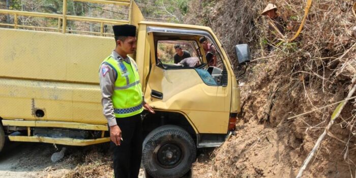Petugas kepolisian berpeci dan berompi hijau memeriksa kondisi truk engkel kuning AE 8177 YF yang ringsek pada bagian pintu kanan usai menabrak tebing tanah di Jalan Raya Pacitan-Ponorogo, Desa Ngreco, Tegalombo.