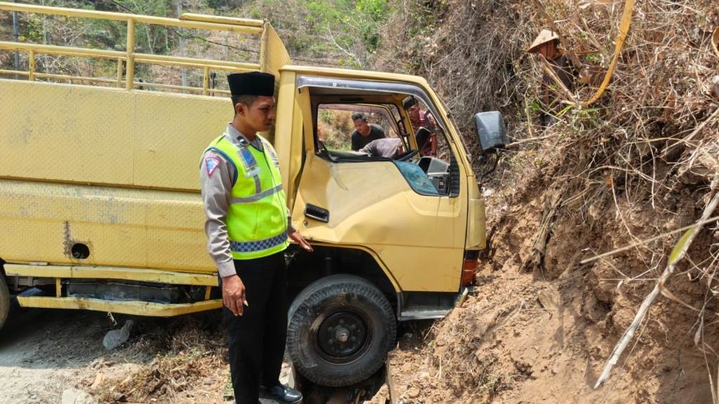 Petugas kepolisian berpeci dan berompi hijau memeriksa kondisi truk engkel kuning AE 8177 YF yang ringsek pada bagian pintu kanan usai menabrak tebing tanah di Jalan Raya Pacitan-Ponorogo, Desa Ngreco, Tegalombo.