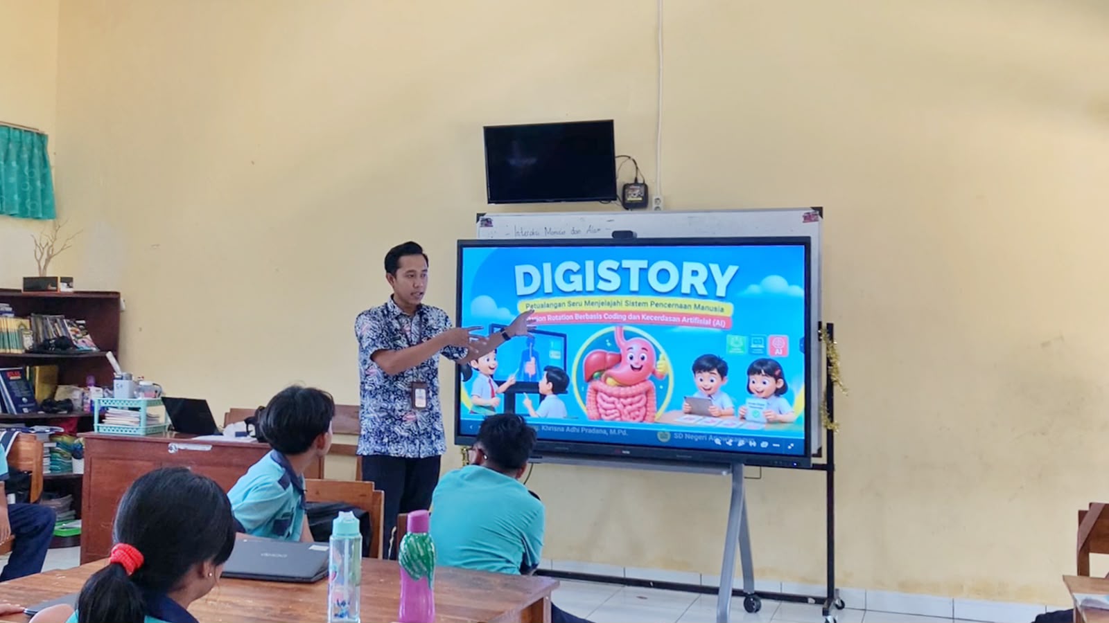Guru SD Negeri Arjowinangun Pacitan Khrisna Adhi Pradana menjelaskan materi sistem pencernaan manusia melalui media interaktif DIGISTORY berbasis coding dan AI pada layar Interactive Flat Panel di depan siswa