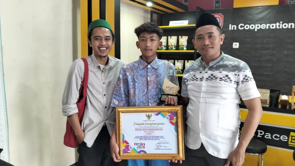 Siswa SMKN 1 Nawangan Regga Widi Adriansyah Tunjukkan Trofi dan Piagam Juara 1 FLS2N Jawa Timur 2026 Siswa SMKN 1 Nawangan Pacitan, Regga Widi Adriansyah (tengah), memegang trofi dan piagam penghargaan Juara 1 FLS2N Tingkat Provinsi Jawa Timur 2026 didampingi dua guru pendamping di Pace Edotel SMKN 2 Pacitan.