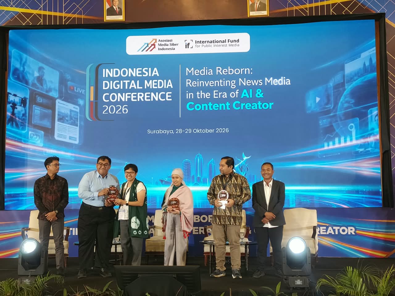 Para narasumber dan perwakilan Asosiasi Media Siber Indonesia berfoto bersama sambil memegang plakat di panggung Indonesia Digital Media Conference 2026, Surabaya.